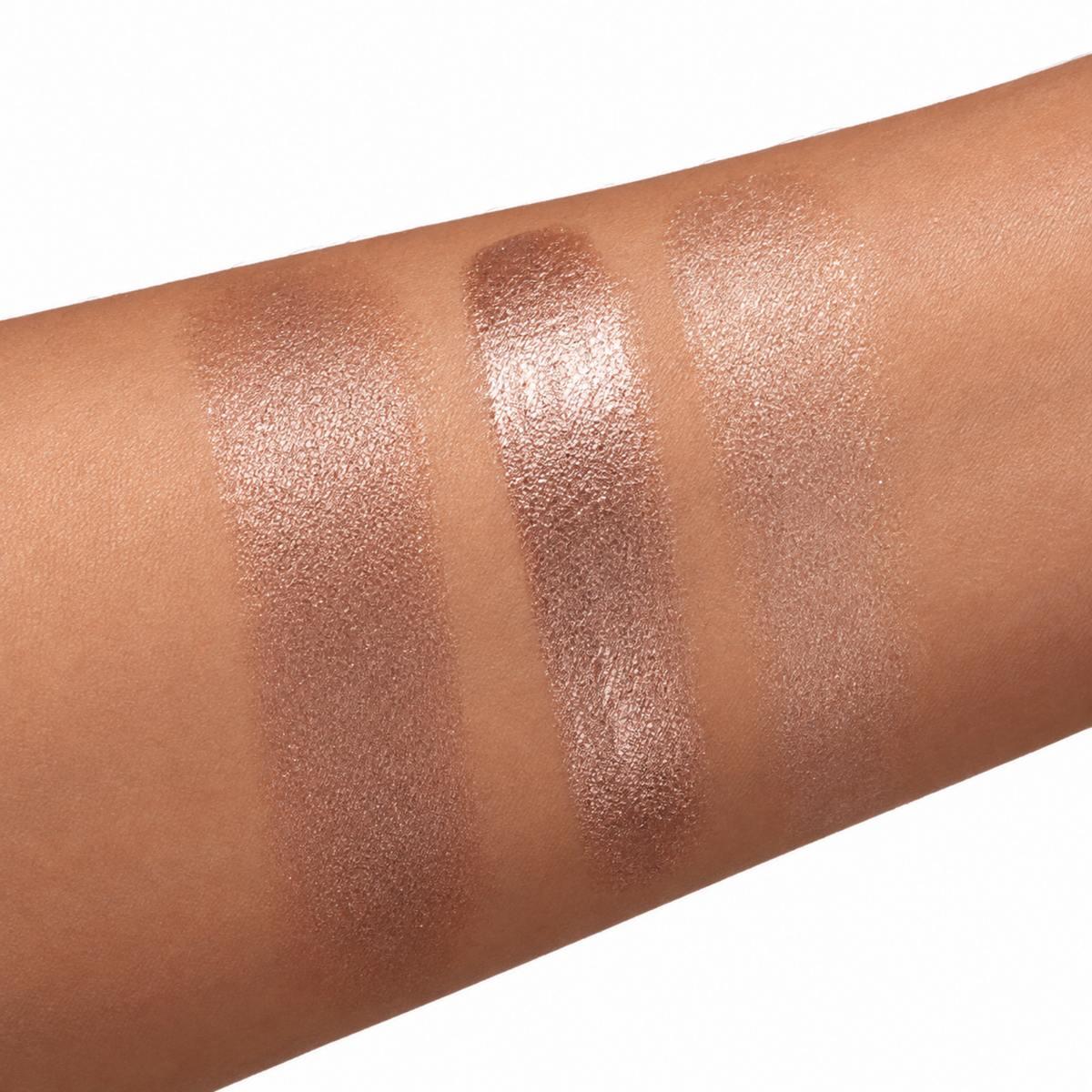 Three vertical makeup swatches on skin showing shimmery rose gold and champagne