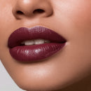Close-up of a person's lips with a dark purple lipstick on a neutral background