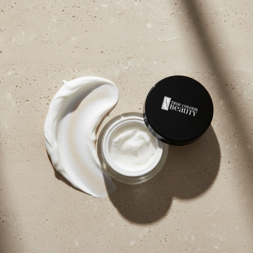Open jar of cream with a swatch on a beige surface, featuring 'True Colour Beauty' brand.