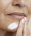 Close-up of a woman applying cream to her face with her finger.