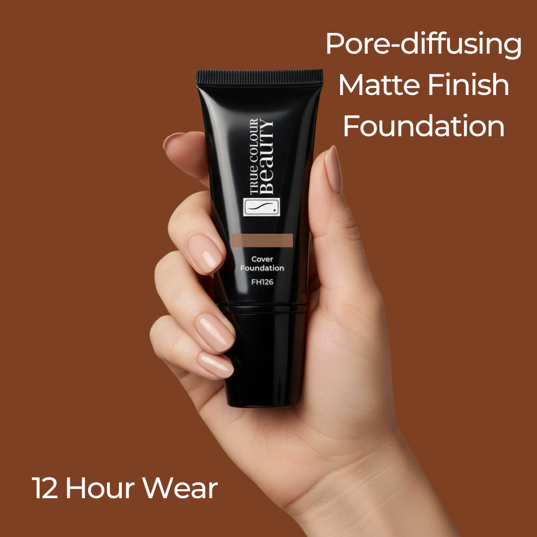 Hand holding a black foundation tube with 'The Colour Beauty' branding on a brown background.