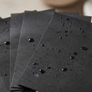 Stack of black blotting paper sheets with water droplets on a blurred background