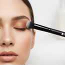 Makeup brush applying cream to a person's face with a blurred background
