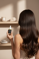 Woman with long, straight hair holding a hair oil dropper bottle in a bathroom setting.