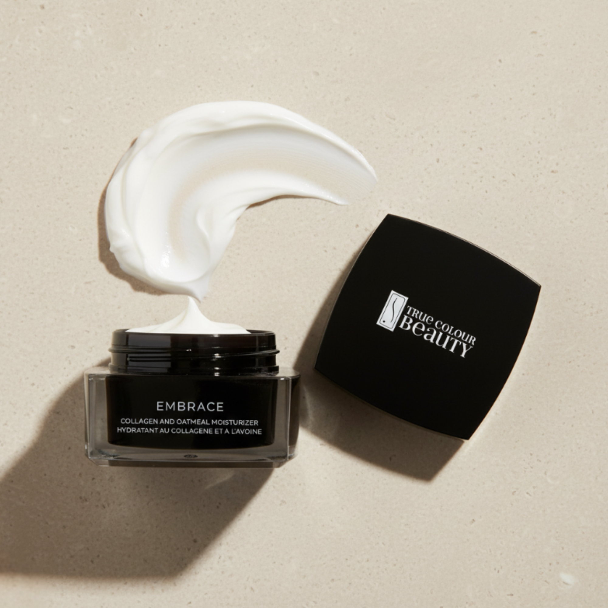 Black jar of Embrace Collagen and Hyaluronic Moisturizer with a swatch of cream on beige background
