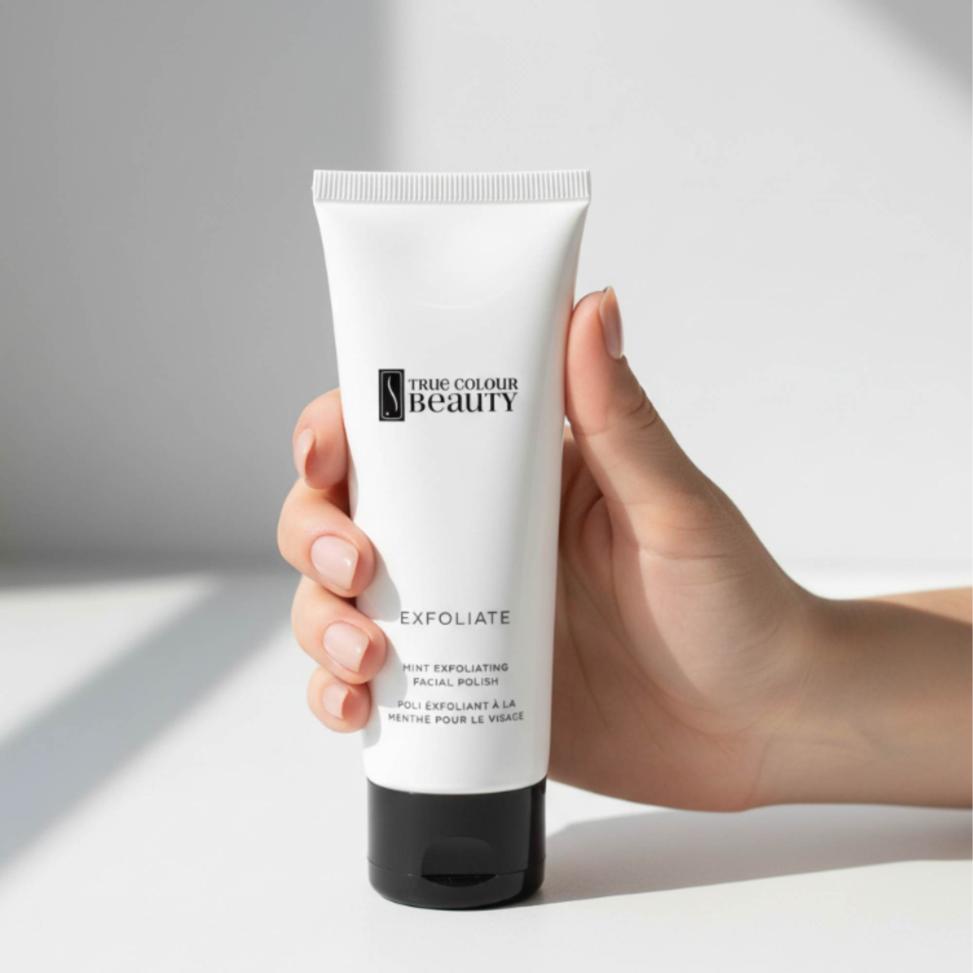 Hand holding a tube of 'True Colour Beauty' exfoliating product on a light background