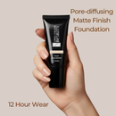 Hand holding a black foundation tube with text about pore-diffusing matte finish foundation on a beige background