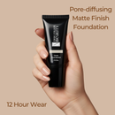 Hand holding a black foundation tube with text about pore-diffusing matte finish foundation on a beige background