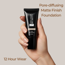Hand holding a black foundation tube with text about pore-diffusing matte finish foundation on a beige background