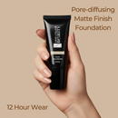 Hand holding a black foundation tube with text about pore-diffusing matte finish and 12-hour wear on a beige background
