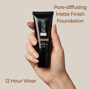 Hand holding a black foundation tube with text about pore-diffusing matte finish foundation on a beige background