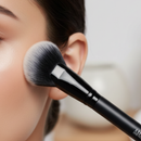 Makeup brush applying powder to a person's face with a blurred background