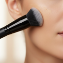 Makeup brush applying powder to a person's cheek with a blurred background