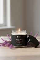 Heather candle with a lit flame on a wooden surface with purple flowers.