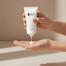 Hand holding a tube of skincare product with cream on a neutral background