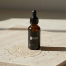 Bottle of True Colour Beauty Rose Gold Oil on a textured surface with soft lighting
