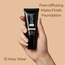 Hand holding a black foundation tube with text about pore-diffusing matte finish and 12-hour wear on a beige background