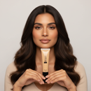 Woman holding a tube of foundation against a neutral background